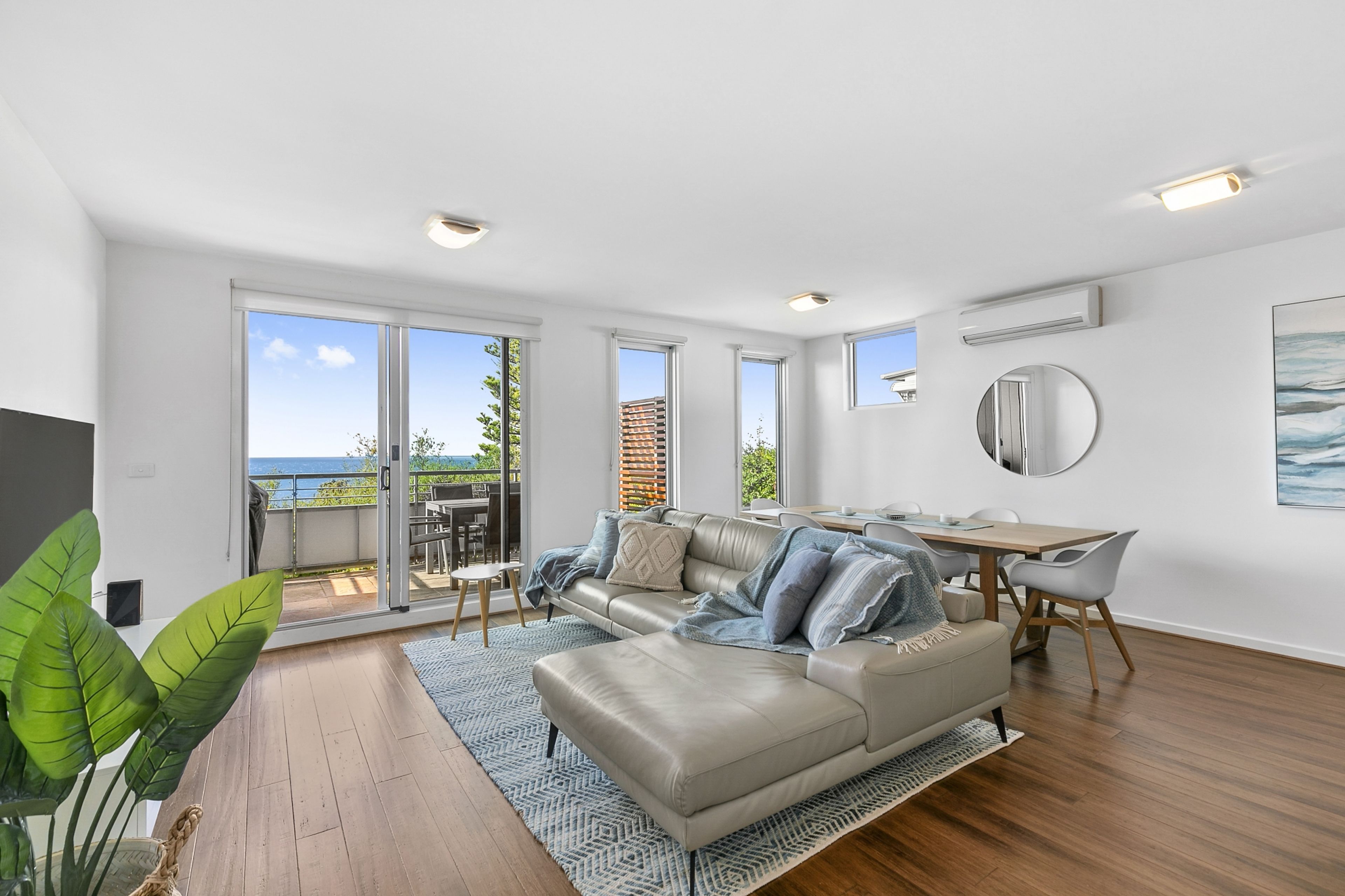 A modern living room with a leather sofa, dining table, and a view of the outdoors.