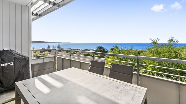 Een balkon met een tafel en stoelen, met uitzicht op de kust.