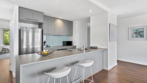 Een moderne keuken met grijze kastjes, een roestvrijstalen koelkast, een centraal eiland met barstoelen, en een magnetron.