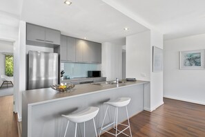 A modern kitchen with grey cabinets, a stainless steel refrigerator, a central island with bar stools, and a microwave.