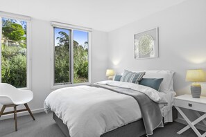 A bedroom with a bed, bedside tables, a chair, and a window with a view of greenery.