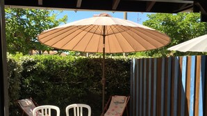 Een overdekt terras buiten, met een tafel, stoelen, een parasol en een houten terras.