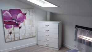 Een slaapkamer met dakraam, een witte dressoir, een kleurrijk sprei en een groot bloemschilderij aan de muur.