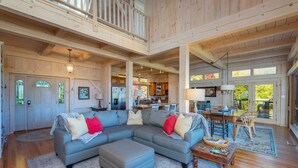 A spacious living area with a large sectional sofa, a wooden coffee table, and a dining table with chairs. - Sky High at Laurel Ridge | Post & Beam Cabin With Long-range Mountain Views! (Black Mountain)