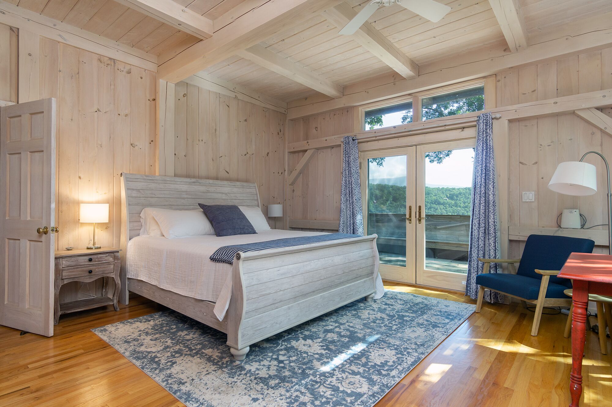 Ein Schlafzimmer mit Holzboden, einem Bett, einem Nachttisch und Blick durch eine Glastür.