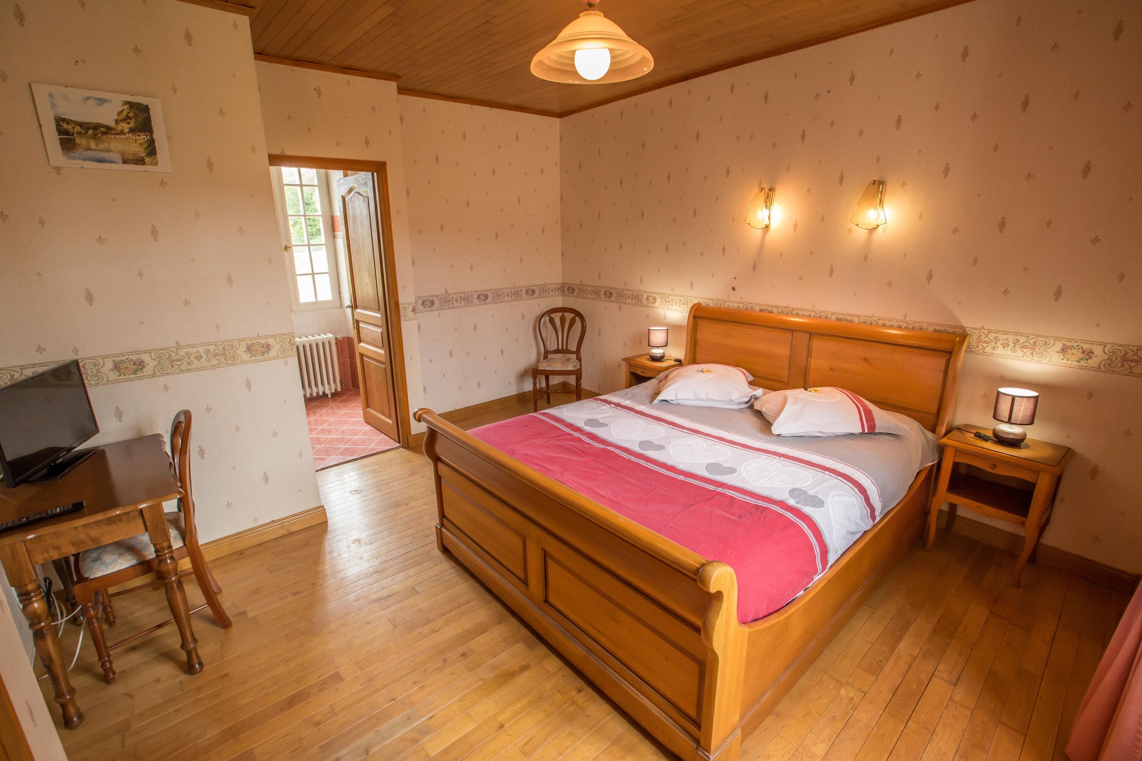 Une chambre avec un lit en bois, un bureau avec une chaise, un radiateur et une fenêtre.