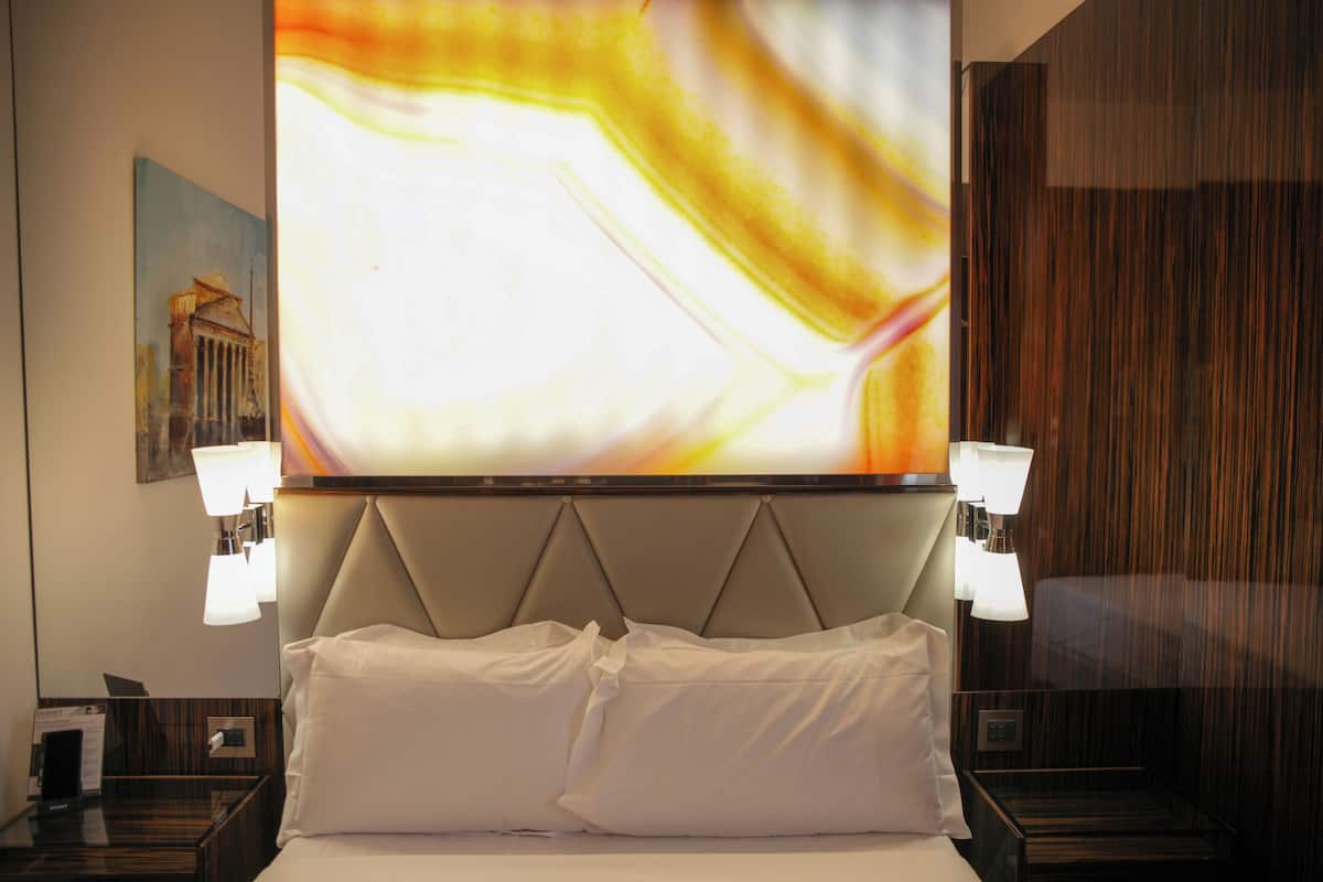 A hotel room with a large bed, two bedside lamps, a wall-mounted TV, and a painting on the wall.