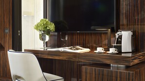 A modern hotel room with a wooden desk, a flat-screen TV, a coffee maker, and a vase with green plants. - Le Boutique Hotel (Rome)
