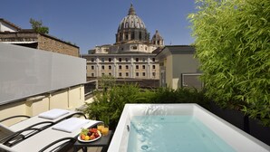 A rooftop terrace with a hot tub, lounge chairs, and a table with fruit and drinks. In the background, there is a large building with a dome. - Le Boutique Hotel (Rome)