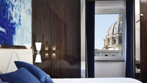 A hotel room with a bed, pillows, a lamp, a painting, and a window with a view of a building. - Le Boutique Hotel (Rome)