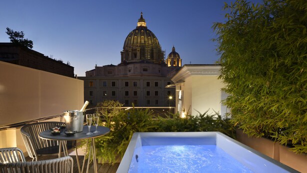 A rooftop terrace with a hot tub, outdoor seating, and a view of a large building with a dome. - Le Boutique Hotel (Rome)