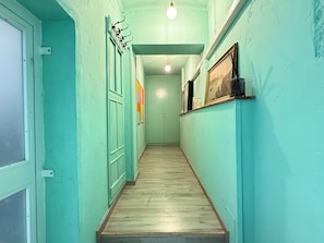 A hallway with teal walls, wooden flooring, and a door on the left.