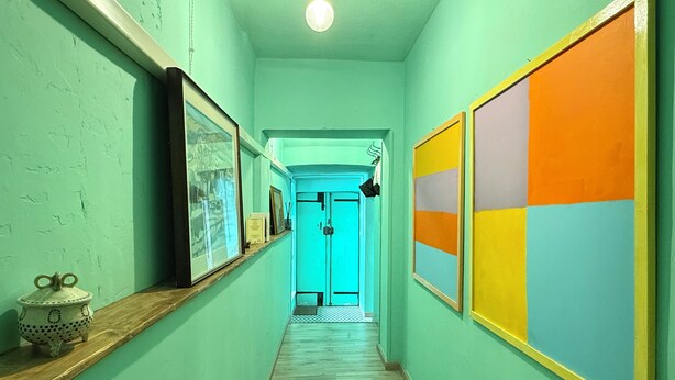 A hallway with framed artwork on the walls, a wooden shelf with decorative items, and a door at the end.