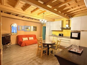 A cozy kitchen with wooden beams, a dining table with chairs, a sofa, and a kitchenette.