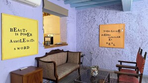A room with a sofa, armchair, and a small table with a vase. There are two motivational posters on the walls.