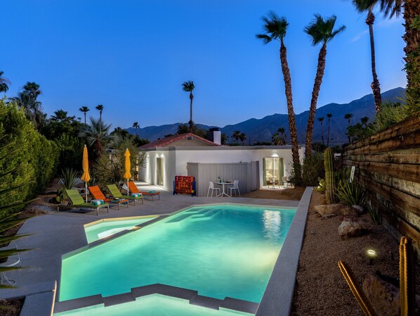 A pool with a clear blue water feature, surrounded by palm trees and a mountain backdrop.