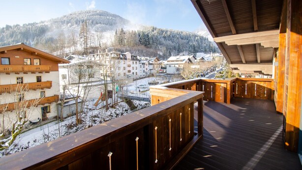 A wooden balcony with a view of a snow-covered village and mountains. - FINEST VILLA Zell am See, luxury, sauna, 12 pax (Zell am See)