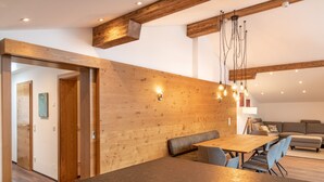 A modern interior with a wooden accent wall, a dining area with a table and chairs, and a seating area with a sofa. - FINEST VILLA Zell am See, luxury, sauna, 12 pax (Zell am See)