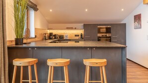 A modern kitchen with a central island, bar stools, and a potted plant. - FINEST VILLA Zell am See, luxury, sauna, 12 pax (Zell am See)