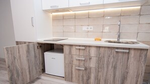 Una cocina compacta con un lavamanos integrado, un refrigerador pequeño y armarios de madera.