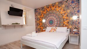 Un dormitorio con cama, televisor de pantalla plana montado en la pared y un tapiz colorido detrás de la cama.
