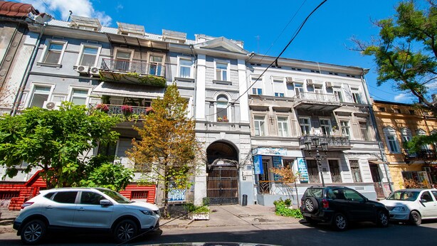 Un edificio de varios pisos con entrada central, balcones y vista a la calle.