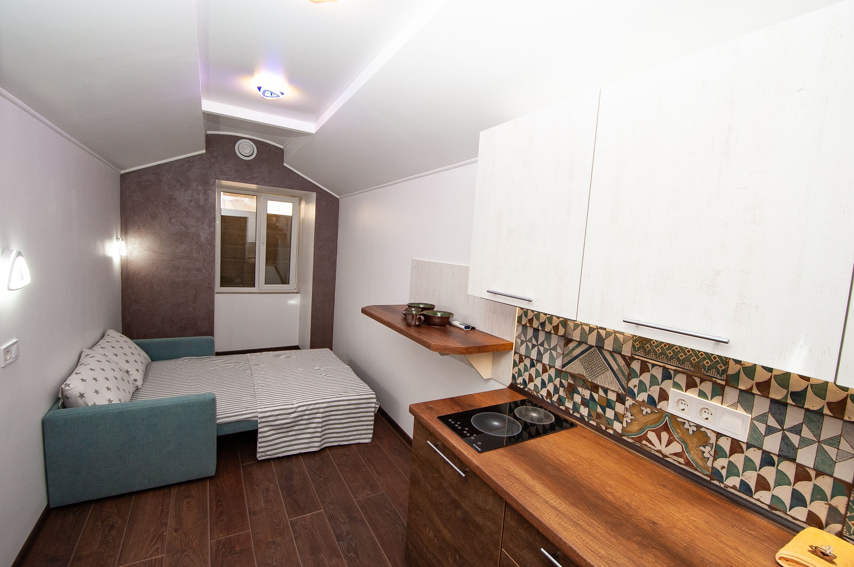 A compact kitchen with a built-in stove, a small seating area with a sofa and a striped blanket, and a window with a view of the outside.