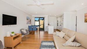 A modern living room with a sofa, TV, and a dining area with chairs and a table. - Villa Zelma - Pet Friendly - 4 Min Walk to Beach (Culburra Beach)