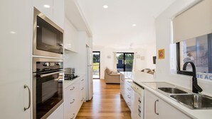 A modern kitchen with white cabinetry, stainless steel appliances, and a wooden floor. - Villa Zelma - Pet Friendly - 4 Min Walk to Beach (Culburra Beach)