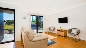 A modern living room with a sliding glass door leading to a balcony, a flat-screen TV mounted on the wall, and two comfortable chairs. - Villa Zelma - Pet Friendly - 4 Min Walk to Beach (Culburra Beach)