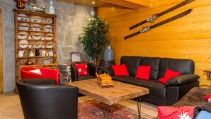 A cozy room with a wooden ceiling, a black leather sofa with red cushions, a wooden table, and a wall-mounted ski rack. - Apartment for 20 people with Wi-Fi, near Linga gondola - Chatel Reservation (châtel)
