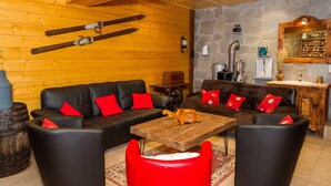 A cozy room with wooden walls, a black leather sofa, red cushions, a wooden coffee table, and a stone wall with a mirror and kitchen appliances. - Apartment for 20 people with Wi-Fi, near Linga gondola - Chatel Reservation (châtel)