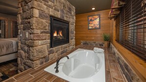 A stone-walled bathroom with a large bathtub, a fireplace, and wooden paneling. - Tennessee Dream (Gatlinburg)