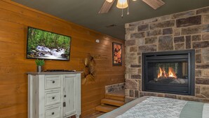 A cozy room with a stone fireplace, a television mounted on a wooden wall, and a white cabinet with drawers. - Tennessee Dream (Gatlinburg)