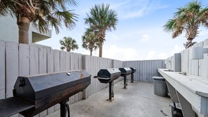 An outdoor barbecue area with multiple grills, a wooden fence, and palm trees.