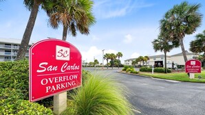 A red parking sign for San Carlos Overflow Parking with a clear view of the surrounding area including palm trees and a building in the background.