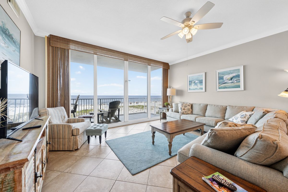 A spacious living room with a large sliding glass door leading to a balcony, a ceiling fan, and a flat-screen TV.