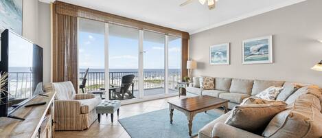 A spacious living room with a large sliding glass door leading to a balcony, a ceiling fan, and a flat-screen TV.