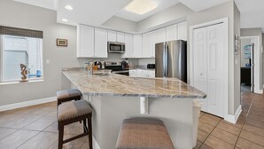 A modern kitchen with white cabinets, stainless steel appliances, and a marble island with bar stools.