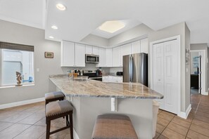 A modern kitchen with white cabinets, stainless steel appliances, and a marble island with bar stools.