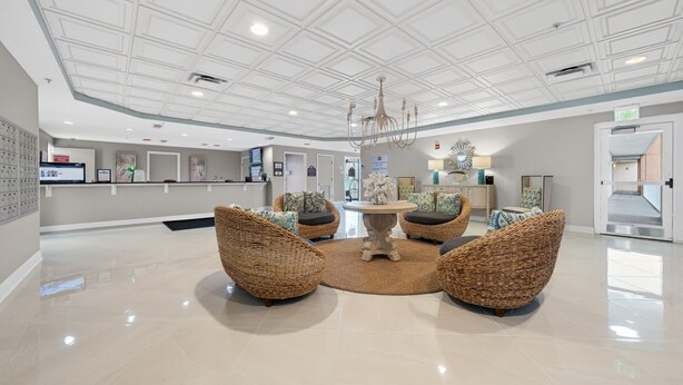 A lobby with a reception desk, wicker chairs, a central table, and a chandelier.