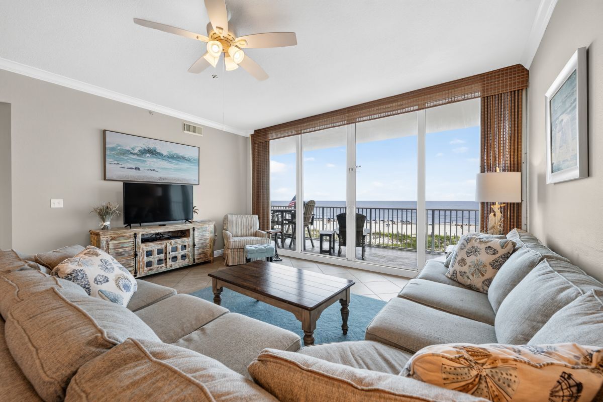 A living room with a sofa set, a coffee table, a television, and a balcony with a view of the sea.