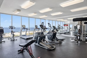 Ein Fitnessraum mit Cardiogeräten, Krafttrainingsgeräten und großen Fenstern mit Meerblick.