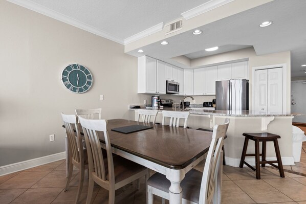 Una cocina moderna con muebles blancos, una isla central y una zona de comedor con una mesa y sillas de madera.