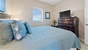 Une chambre à coucher avec un lit, une commode, un téléviseur et une fenêtre avec des stores.