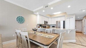 Une cuisine moderne avec des meubles blancs, un îlot central et un coin repas comprenant une table et des chaises en bois.