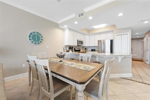 Una cocina moderna con armarios blancos, una isla central y un comedor con mesa y sillas de madera.