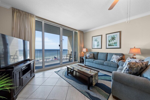 A living room with a television, sofa, and coffee table, a balcony with a view, and two framed pictures on the wall.