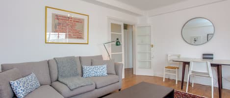 A modern living room with a grey sofa, a coffee table, a desk with a chair, a round mirror, and a framed poster on the wall.
