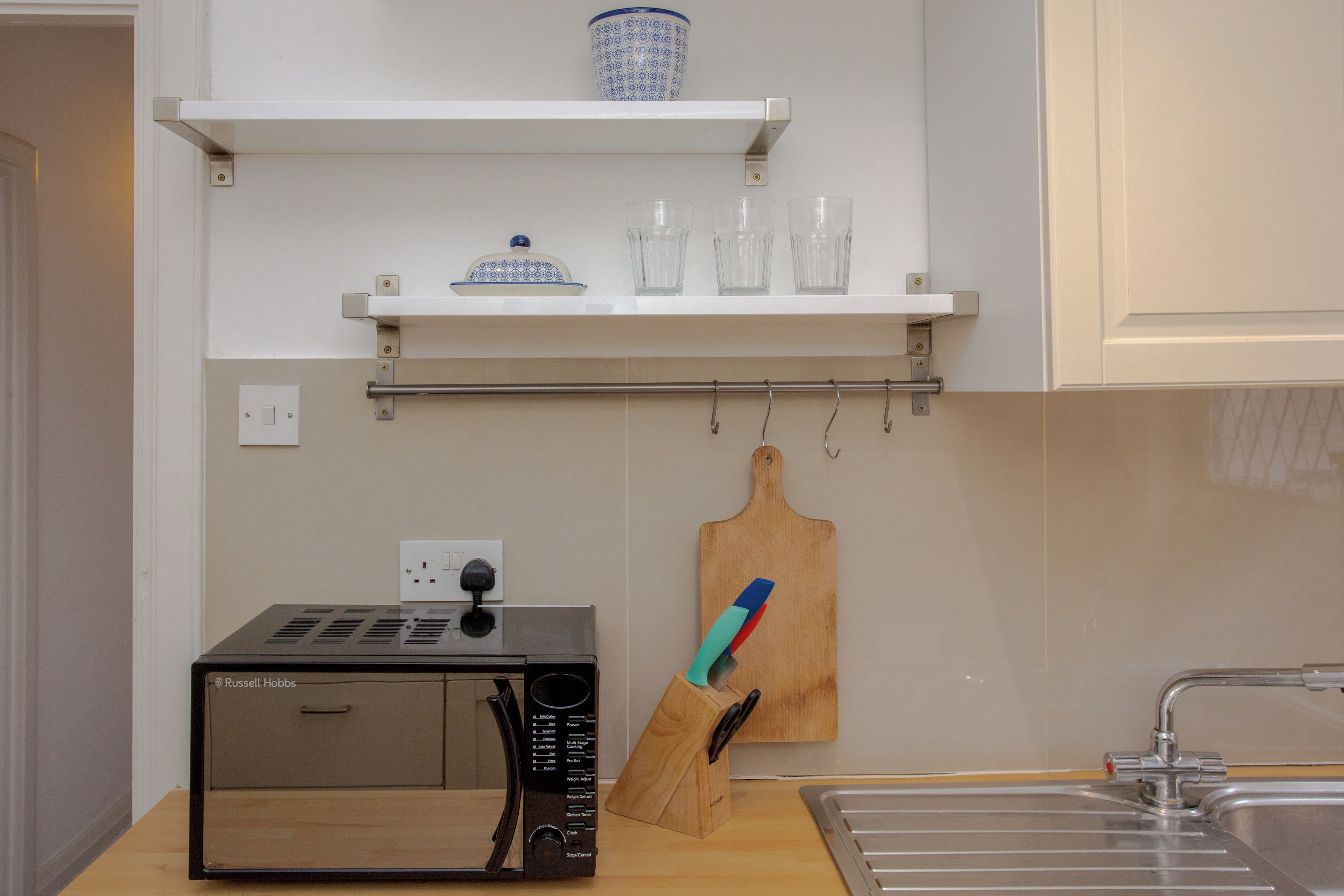 A kitchen with a microwave, a knife block, and a shelf with glassware.